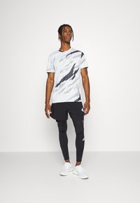 Men's athletic outfit featuring a white and black patterned short-sleeve shirt, black shorts, and black leggings, paired with white shoes.