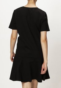 Robe noire à manches courtes, haut ajusté et jupe évasée. Fabriquée en tissu lisse avec un design simple et épuré, sans motifs ni accents visibles.