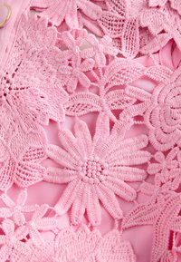 Tissu rose présentant une broderie crochet florale détaillée avec différentes formes de fleurs et des points texturés.