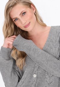Grijze kabelgebreide cardigan met een V-hals, geribde manchetten en twee knopen aan de voorkant. Zachte textuur met een losse pasvorm voor comfort.
