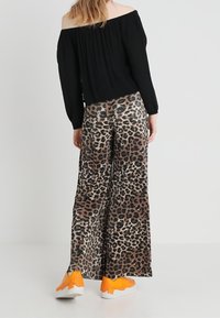 Musta olkapäiden yli menevä paita, leveät leopardikuvioiset housut beigen ja ruskean sävyissä, sekä oranssit lenkkarit valkoisilla pohjilla. Rentoa asua takaa.