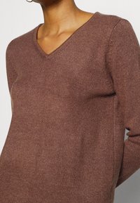 Brun stickad tröja med V-ringning, med en mjuk textur och långa ärmar, som har en något lös passform.
