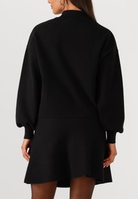 Abito in maglia nera con colletto alto, maniche lunghe a sbuffo e gonna svasata. Texture liscia, design minimalista, senza pattern o accenti visibili.