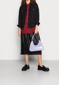 Giacca di jeans nera, camicia a scacchi rossi, gonna nera plissettata, borsa in pelle stampata coccodrillo lavanda e scarpe con plateau nere.