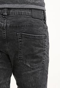 Jeans en denim noir avec une finition délavée. Présente un design classique à cinq poches et une couture visible. Tissu texturé avec une étiquette en cuir de marque.