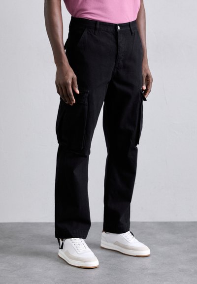Pantaloni cargo negri cu buzunare laterale, material din bumbac, cu picioare ușor conice. Asortați cu adidași albi și un tricou roz.