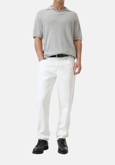 Polo grigio a maniche corte con finitura texture, abbinato a jeans bianchi a gamba dritta e scarpe nere stringate; dettaglio del colletto sottile visibile.