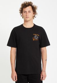 T-shirt en coton noir avec un petit logo Volcom orange sur la poitrine. Coupe classique avec manches courtes et col rond.