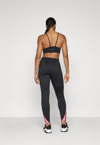 Svart atletisk sports BH med tynne stropper, parret med svarte leggings med rosa detaljer ved anklene, designet for aktiv bruk.