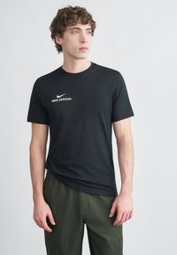 Crna majica od pamuka, s bijelim Nike logotipom i natpisom „NIKE OFFICIAL“ sprijeda. Kratki rukavi, okrugli izrez na vratu.