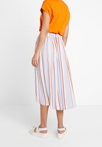 Oranžový top s krátkým rukávem; bílá midi sukně s vertikálními červenými pruhy; bílé sandály na plochém podpatku. Elastický pas; hladká textura látky.