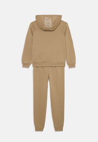 Ensemble en sweatshirt et joggers en coton beige avec capuche, featuring un grand logo blanc "NIKE" au dos du hoodie. Texture douce et lisse.