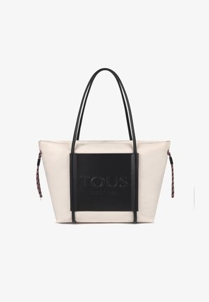 Bolso tote grande, de tela color crema con panel de cuero negro. Cuenta con el logotipo "TOUS" en relieve, asas largas negras y un tirador de cremallera con patrón.