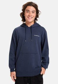 Sudadera con capucha de color azul marino, hecha de algodón. Incluye un bolsillo frontal y un logo simple en el pecho. Textura suave y diseño de corte relajado.