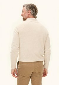 Beige trui met een hoge kraag en ribgebreide manchetten, gemaakt van een zacht textuurmateriaal. Het model draagt lichtbruine corduroy broeken.