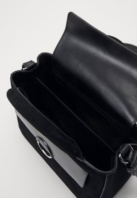 Schwarze Handtasche mit einem Außenmaterial aus Wildleder und Leder, Klappenverschluss mit einem runden Hardware-Akzent und mehreren Innenfächern.