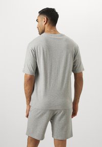 Camiseta de algodón gris de manga corta con un corte holgado, combinada con pantalones cortos gris a juego. La tela parece suave con una textura lisa.