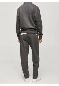 Sweatshirt et pantalon de survêtement gris en tissu doux, avec une coupe décontractée et des poignets côtelés ; complété par des baskets blanches.