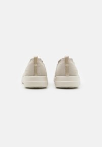 Chaussures de sport beiges avec une tige en mesh respirant, une semelle lisse et une languette à l'arrière pour un enfilage facile.