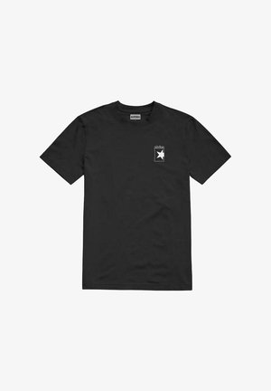 Camiseta de algodón negra con un pequeño gráfico blanco que presenta una estrella dentro de un contorno rectangular en la parte izquierda del pecho. Mangas cortas.