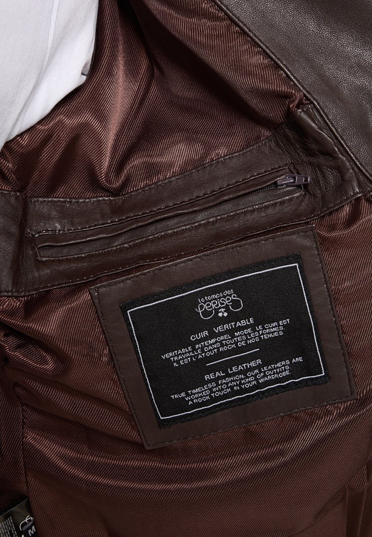Interior van een leren jas in bruin met een gladde textuur, een ritssluiting zak en een zwart label met witte tekst met informatie over het materiaal en onderhoudsinstructies.