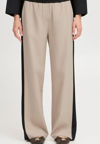 Pantalons larges beiges avec un panneau latéral noir, dotés d'une taille élastique et d'une texture douce et lisse. Comprend des détails subtils de poches avant.