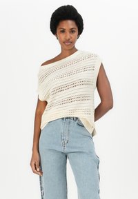Off-white, åpen strikket topp med horisontale striper, korte ermer og asymmetrisk halslinje, sammen med lyseblå høyhente jeans.