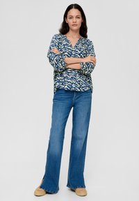 Bloemrijke top in marineblauw en crème, met een V-hals en driekwartmouwen. Loszittende blauwe jeans met een lichte flare aan de onderkant.