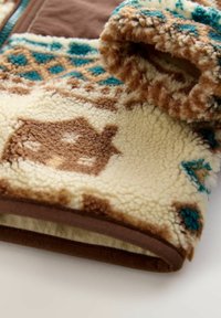 Manche de vêtement en polaire douce avec des motifs géométriques et de maisons en marron, teal et écru, et un bord en marron.