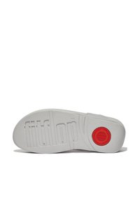 Witte rubberen schoenenzool met verheven "fitflop" logo, textuur oppervlak, cirkelvormige rode accent, en groeven voor grip.