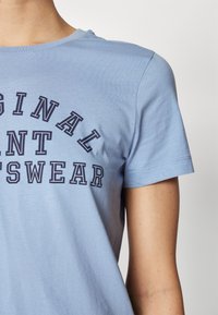 T-shirt di cotone azzurro con maniche corte, caratterizzato da un design testuale blu navy che recita "ORIGINAL PAINT SWEATSHIRT" in diversi caratteri.