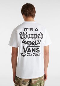 Witte katoenen t-shirt met een grote zwarte grafische print op de achterkant met tekst en patronen, gecombineerd met camouflageprint shorts.