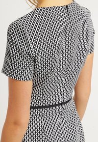 Robe à motif noir et blanc avec manches courtes, taille cintrée et encolure ronde. Accentuée d'une ceinture noire à la taille.