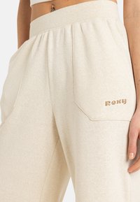 Helle beige Sweatpants aus weichem Stoff, mit einem hohen Bund, Seitentaschen und einem kleinen "ROXY"-Logo auf der Gesäßtasche.