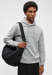 Hoodie grigio in cotone con logo, dotato di cordini e tasca a marsupio. Tiene una borsa a tracolla in tessuto trapuntato nero con una tracolla ampia.