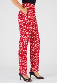 Rode gebloemde pantalons met witte bloemenontwerpen, rechte snit, zijzakken en een textuurstof; gecombineerd met zwarte open teen hakken.