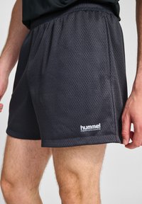 Svarta mesh idrottshorts med elastisk midja och logo på nedre vänstra sidan. Har en andningsbar textur och en lös passform.
