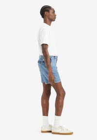 Shorts din denim de culoare albastru deschis, cu un design relaxat și buzunare la spate, asortați cu un tricou alb cu guler rotund și adidași crem cu talpă bej.