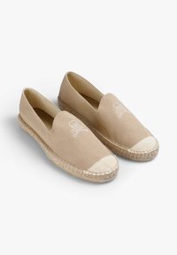 Beige canvas espadrilles met geweven jute zolen. Voorzien van een witte doodskop met gekruiste botten geborduurd op de voorkant. Gesloten achterkant ontwerp.