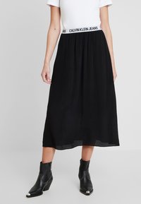 Gonna midi nera con fascia elastica di Calvin Klein Jeans, realizzata in tessuto leggero. Abbinata a stivaletti neri alla caviglia.