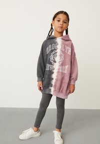 Bluza z kapturem z gradientem od ciemnoszarego do jasnoróżowego, z białym napisem „BROOKLYN” i „NEW YORK”, połączona z szarymi legginsami.