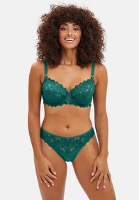 Ensemble de lingerie en dentelle verte avec des bords festonnés, comprenant un soutien-gorge avec des bretelles réglables et une culotte assortie, tous deux finement détaillés.