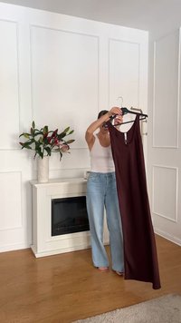 Lang bordeauxkleurige jurk aan een hanger met een ronde hals en subtiele uitsnijdetails. De stof lijkt glad en soepel. Achtergrond met een lichte houten vloer.