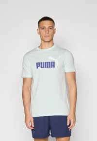 Šviesiai mėlyna medvilninė marškinėliai su dideliu tamsiai mėlynu "PUMA" logotipu ir baltu puikiai puma siluetu kairėje pusėje. Trumpomis rankovėmis ir apvaliu iškirpimu.