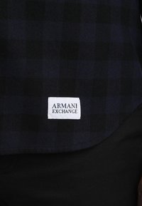 Navyblauwe geruite overhemden met een wit label waarop "ARMANI EXCHANGE" in zwarte tekst staat, ontworpen met een casual pasvorm en zachte stof.