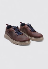 Zapatos de cuero marrón con un diseño de cordones azul marino y una suela de goma beige con detalles texturizados. Logo situado en la lengüeta.