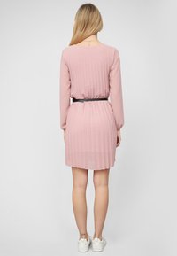 Abito a pieghe di un tenue rosa pallido con maniche lunghe, vita cintrata e cintura nera. Tessuto liscio, lunghezza al ginocchio, design a strati con finitura trasparente.