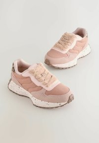 Różowe sneakersy z teksturowaną cholewką i puszystym paskiem, o zakrzywionym kształcie, z oddychającego materiału oraz nakrapianą białą podeszwą.