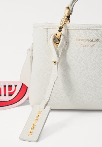 White leather handbag with textured finish, gold-tone hardware, and logo detail. Features a matching tag and a pink and black strap.