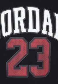 Maillot noir avec "JORDAN" en texte blanc en haut, numéroté "23" en rouge entouré de gris, fabriqué en tissu texturé.